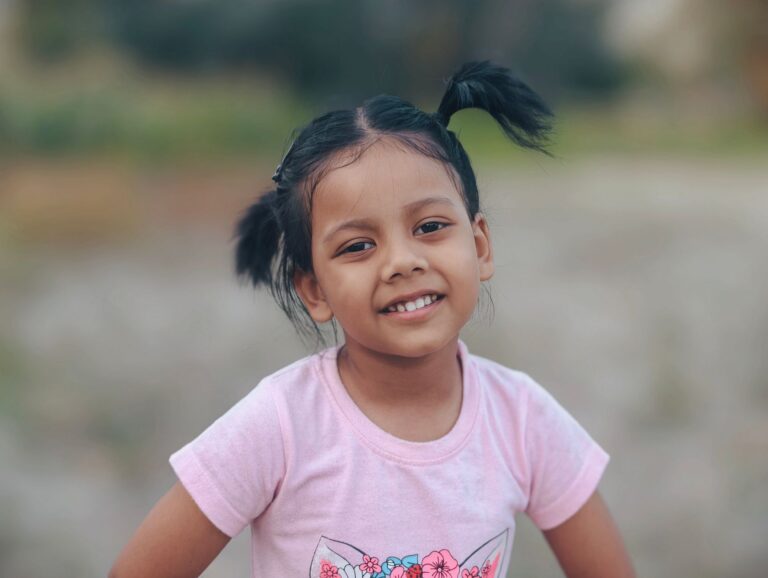 A smiling young girl with pigtails outdoors.