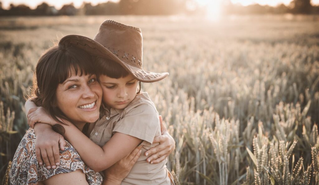 A smiling mother hugging her young son in a sunlit field.